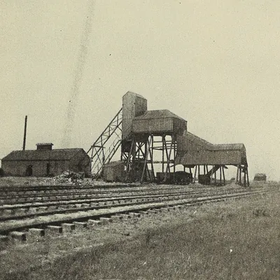 A small wooden tipple with an inclined trestle and a low brick engine house beside several railroad sidings on open prairie.