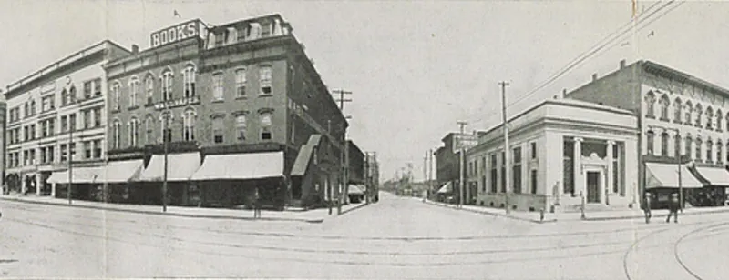 A wide panoramic street scene of downtown Jackson: brick business blocks with awnings, streetcar tracks curving through a broad intersection, a man on a bicycle and people on the sidewalks.