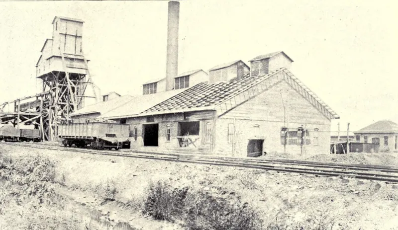 A coal mine at Virden: a tall wooden tipple and headframe at left with coal cars beneath, a brick smokestack, and a long brick engine house beside railroad tracks.