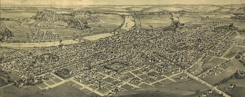 A bird's-eye drawing of Canal Dover laid out in a grid of streets and houses beside the winding Tuscarawas River, with smoking factory chimneys and bridges along the water and farm hills beyond.